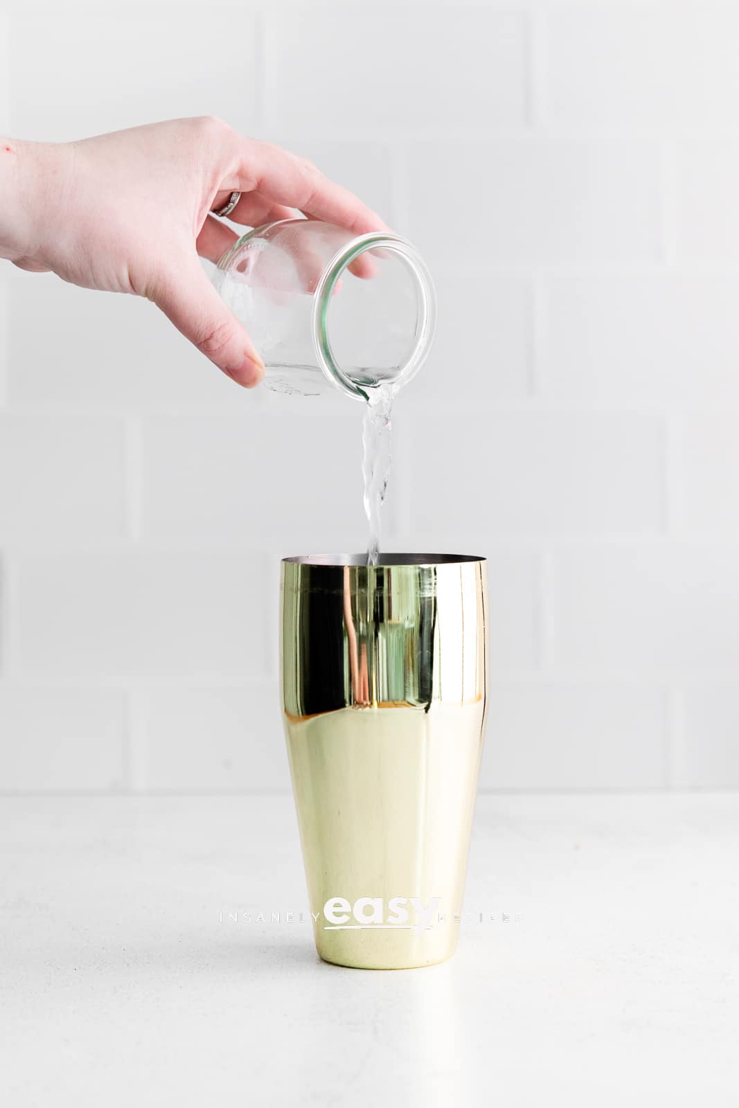 clear liquid being poured into golden cocktail shaker