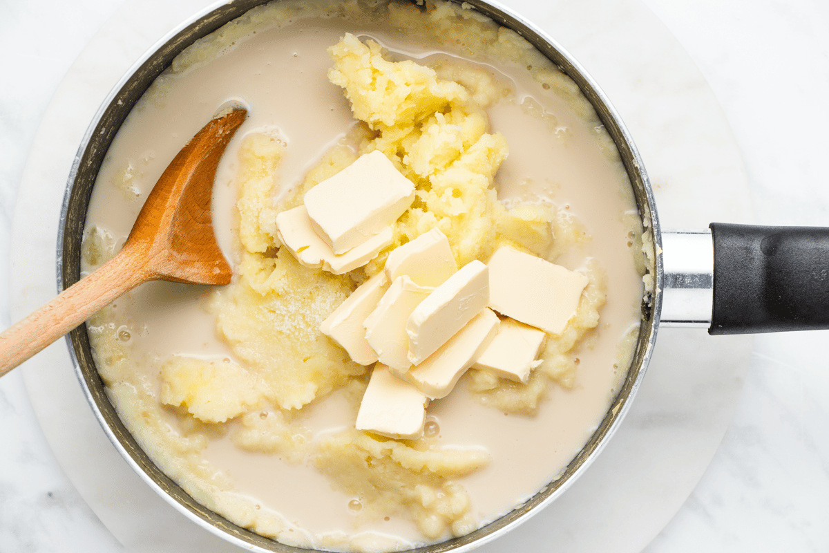 dairy free mashed potatoes with vegan butter slabs, milk liquid and wooden spoon in pot