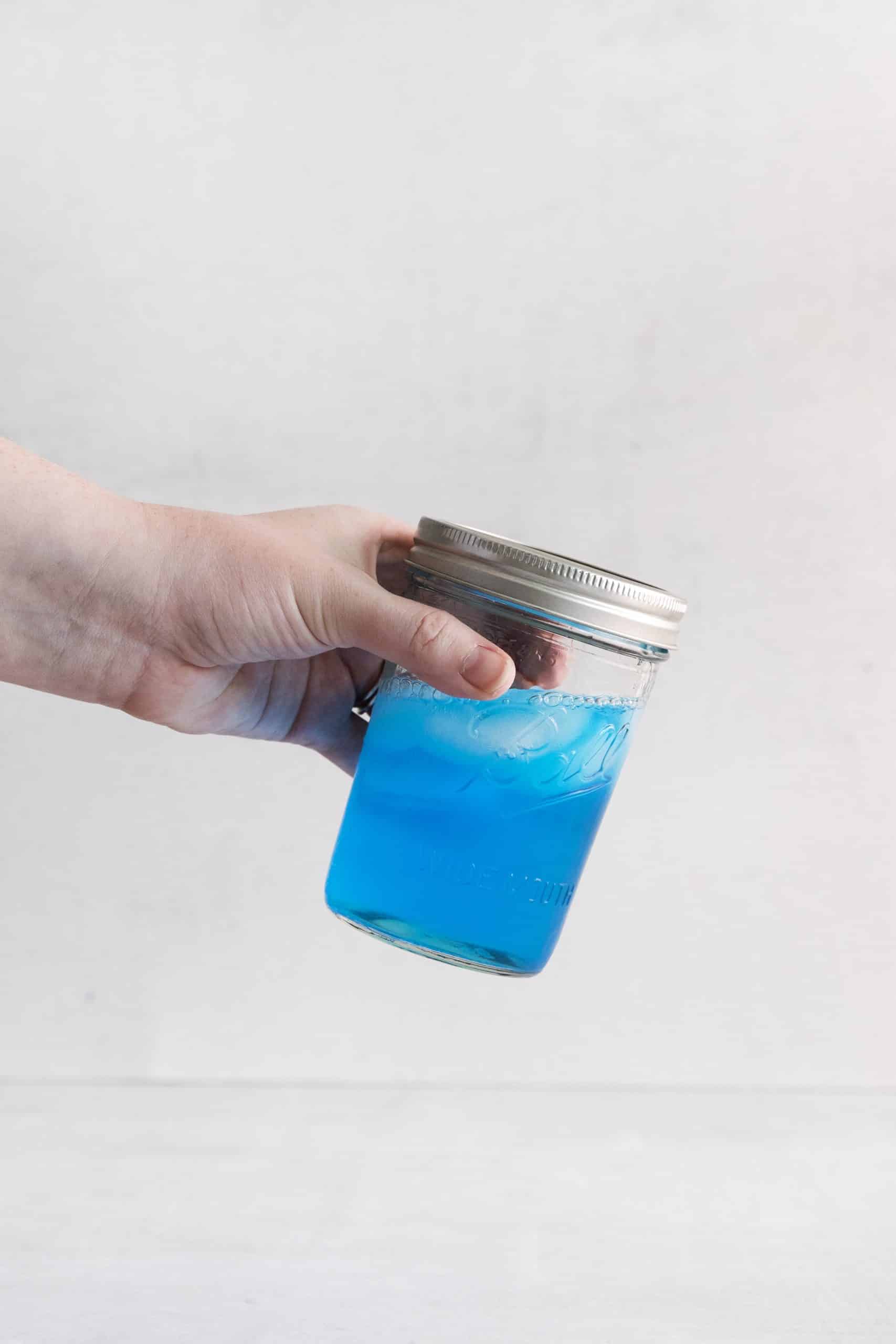 hand shaking ball jar filled with blue liquid