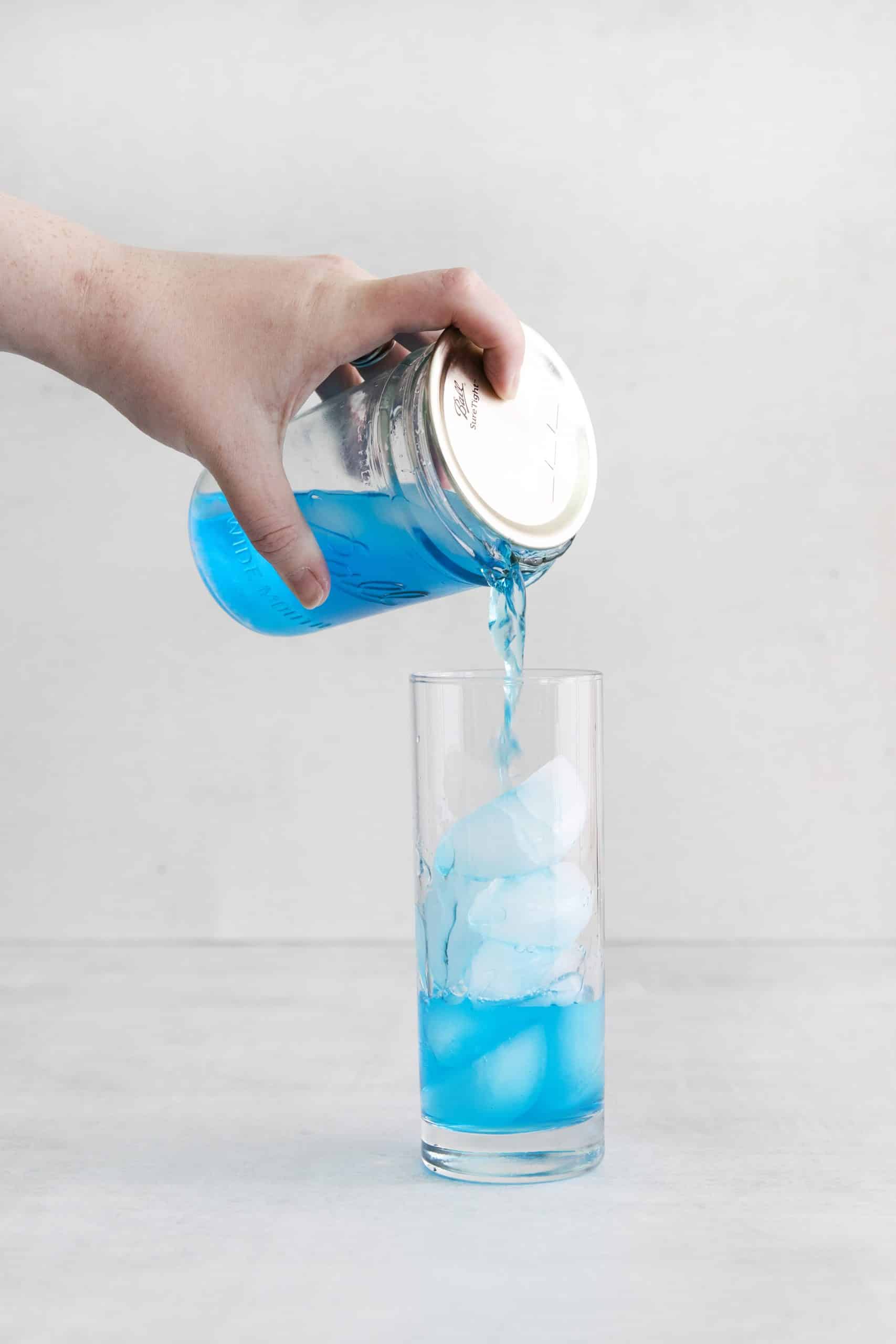 ball jar pouring blue liquid out into a tall glass