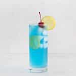 tall clear glass with blue liquid and ice cubes A lemon wheel on top and a cherry