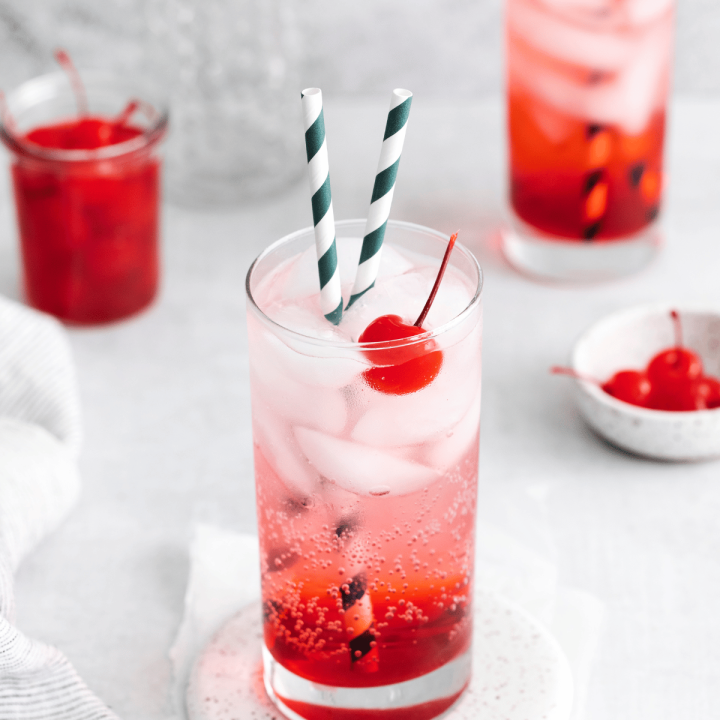 Kiddie Cocktail Drinks - two tall clear glasses with red and clear fizzy liquid with cherry and straws in the glass