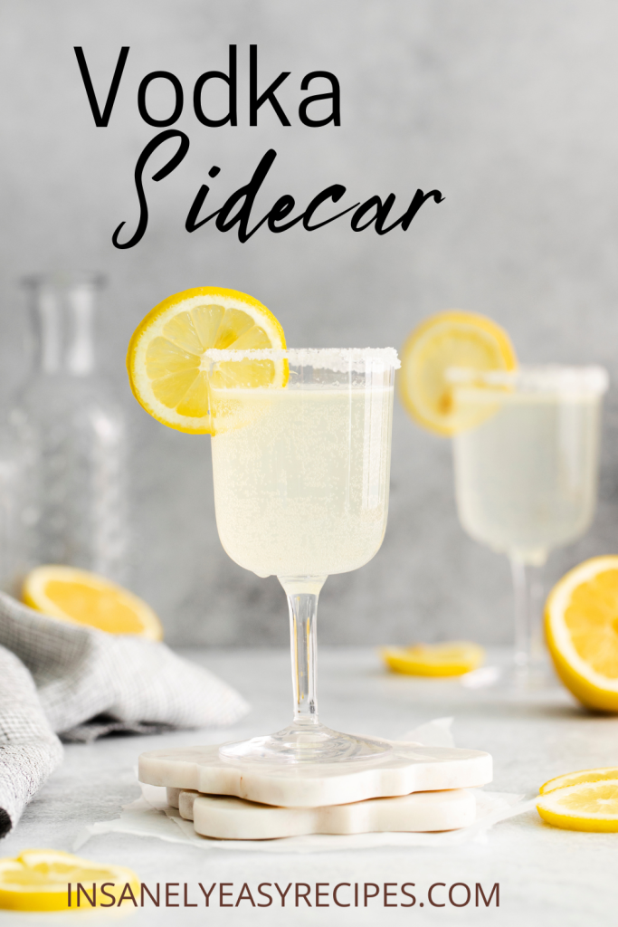 two wine shaped glasses of yellow liquid with lemon wheels on glasses and on surface, grey linen to back left with text overlay vodka sidecar