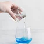 clear liquid being poured into a glass with blue liquid