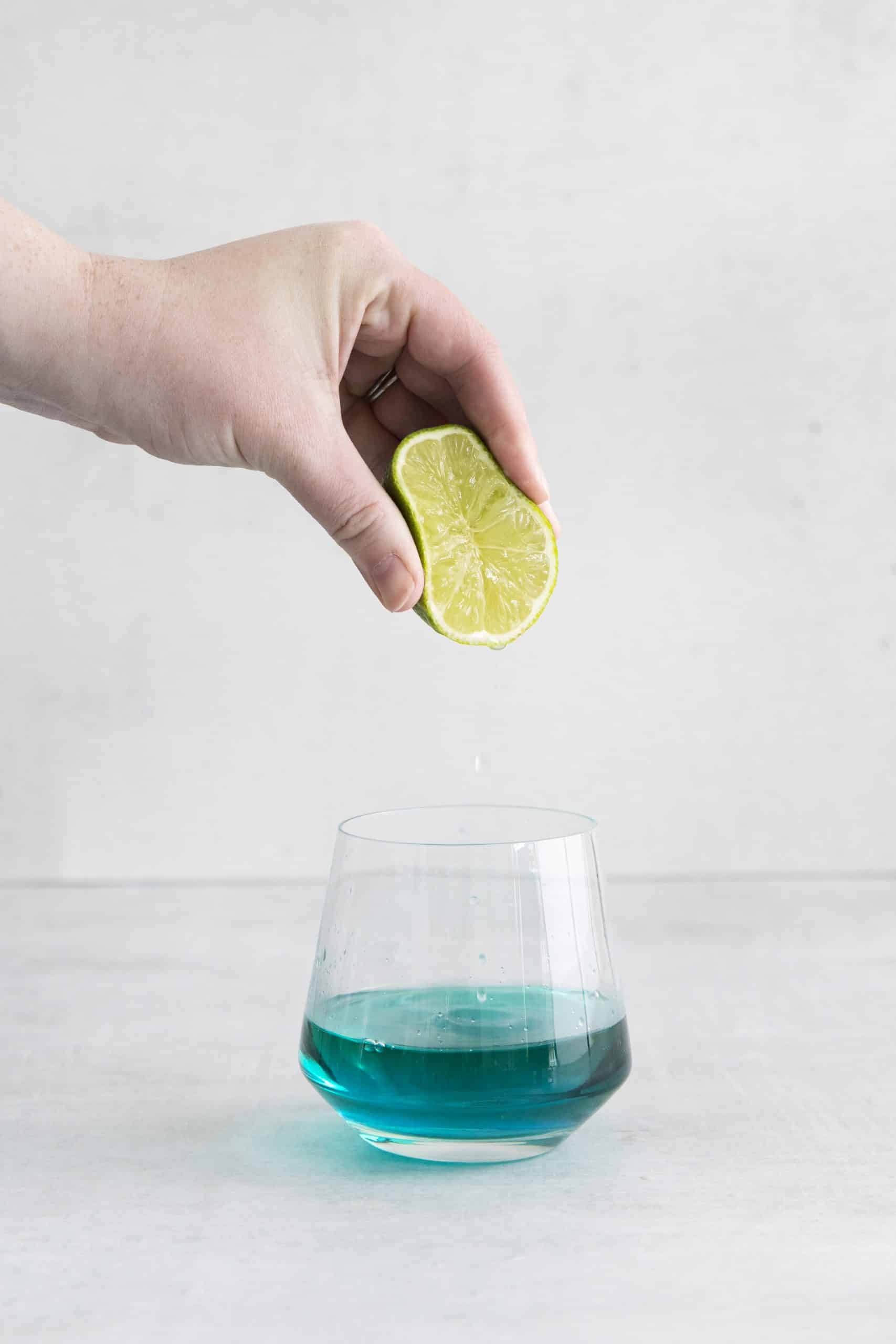 lime being squeezed into a glass with green liquid