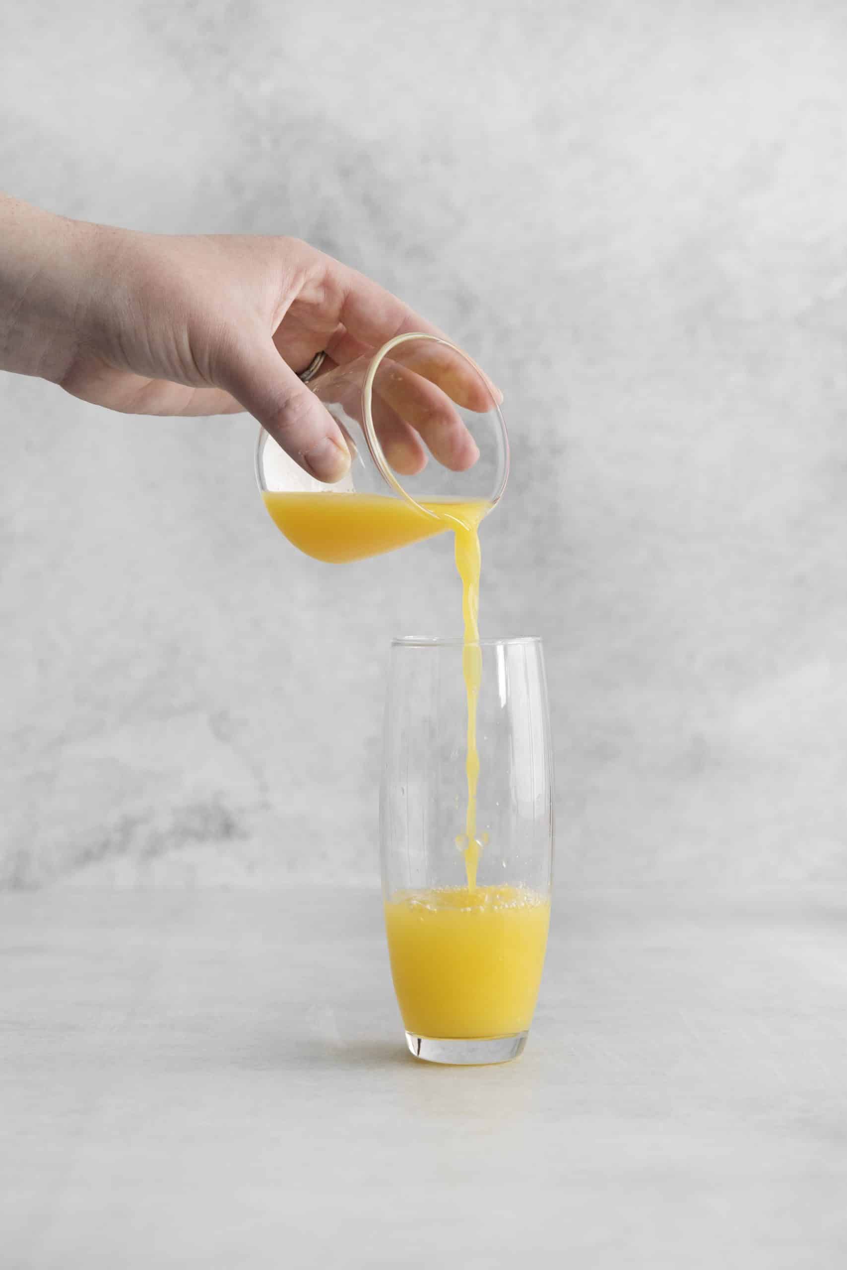 orange juice being poured into a tall glass