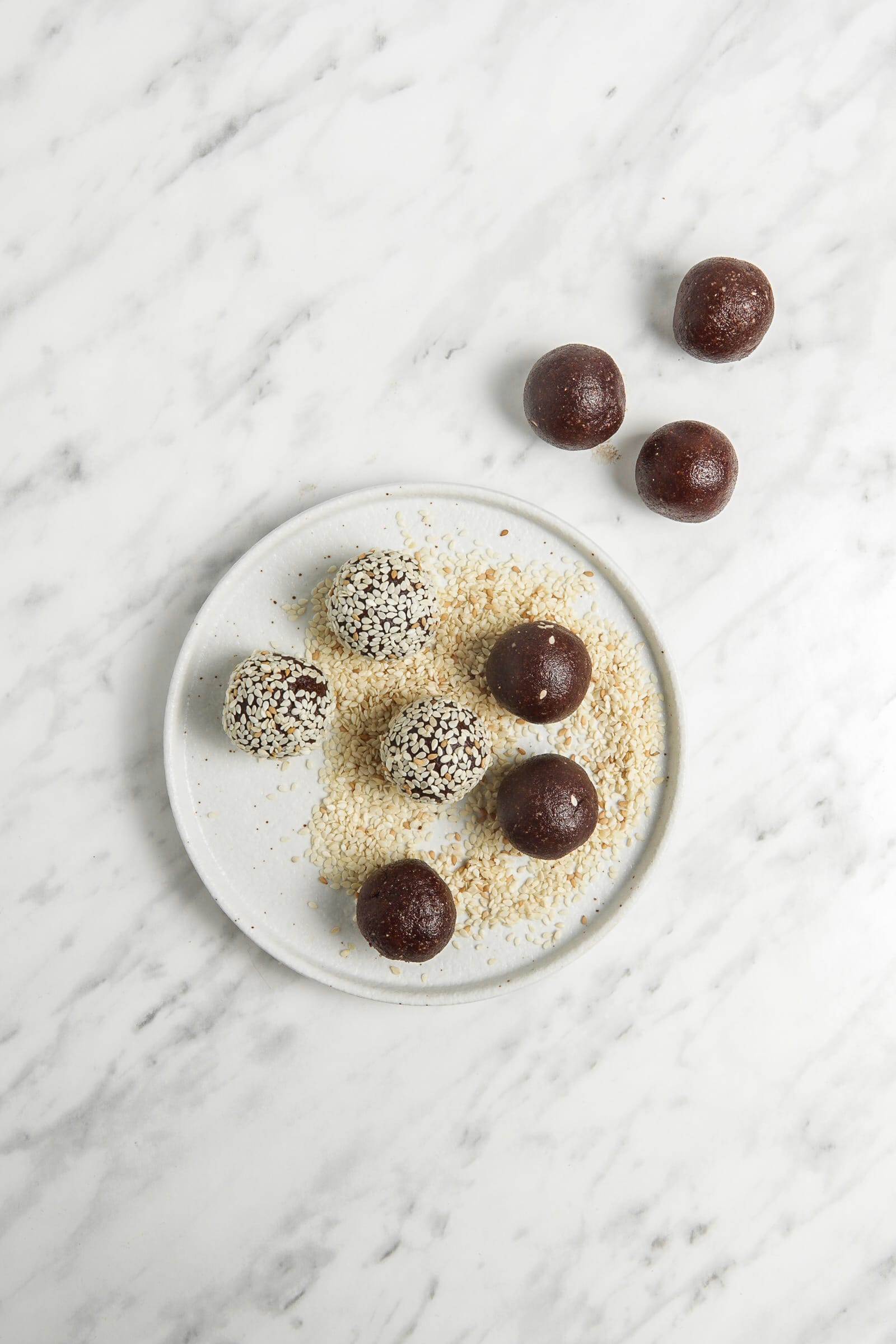 top view photo of 9 bliss balls, being coated in sesame seeds on a plate of seasame seeds