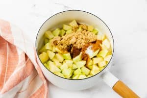 green apples diced, in a white saucepan with brown sugar and spices on top