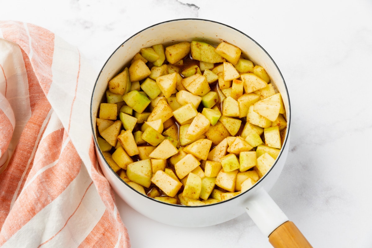 green apples in white saucepan with brown sugar mixed in