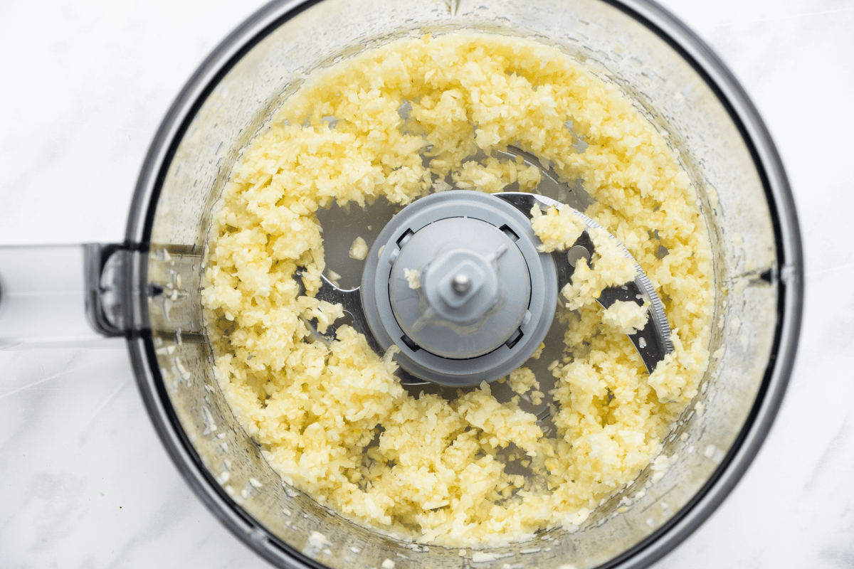 top view photo of garlic cloves and onion in a food processor, chopped until fine