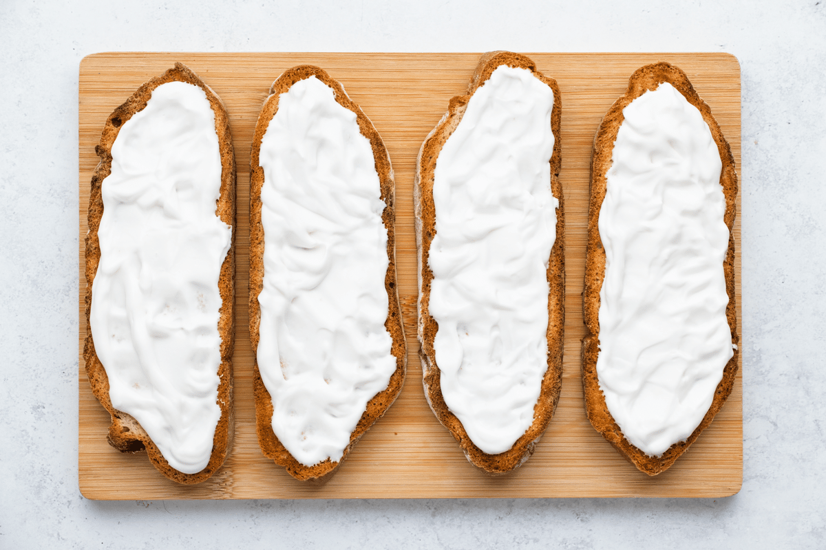 top view photo of 4 toasted sourdough bread slices with yogurt spread on top, on a wooden cutting board