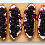 top view photo of 4 toasted sourdough bread slices with yogurt and blueberry jam spread on top, on a wooden cutting board