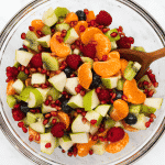 clear glass bowl of christmas fruit salad with wooden spoon in it