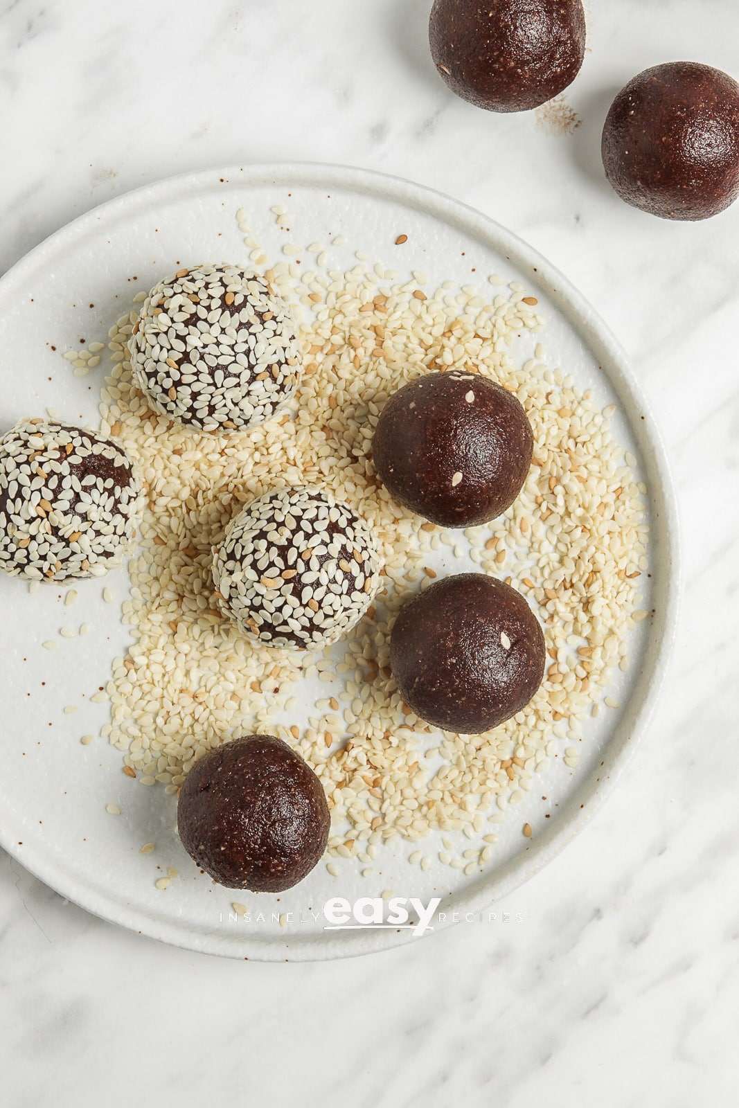 top view photo of 8 bliss balls, being coated in sesame seeds on a plate of sesame seeds