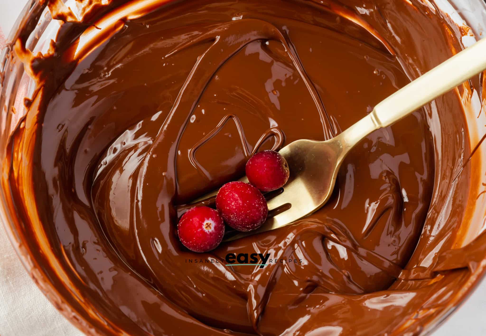 a fork holding three cranberries, dipping them into melted chocolate.