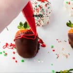 person decorate brown chocolate covered strawberry with red pipping