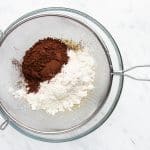 photo of dry ingredients (flour and cocoa powder) being sifted into a glass bowl