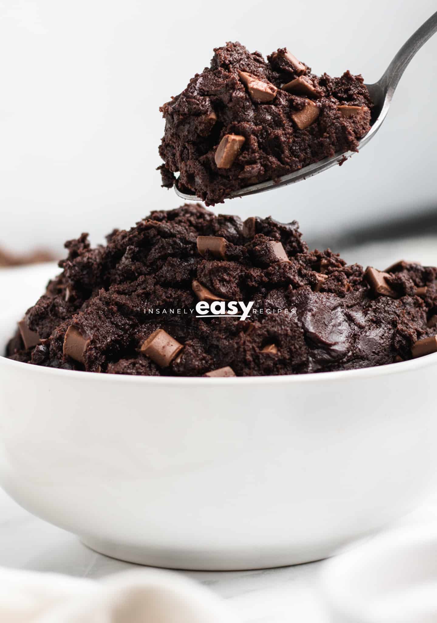 photo of edible brownie batter in a white bowl with a silver spoon scooping out some of the batter