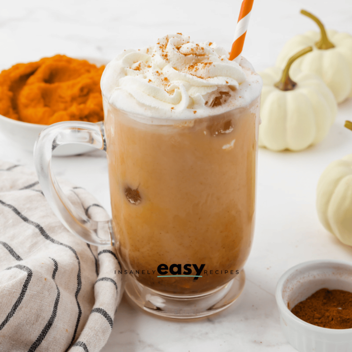 pumpkin spice latte in a clear mug with pumpkin puree in the back left and white pumpkins in the back top right.