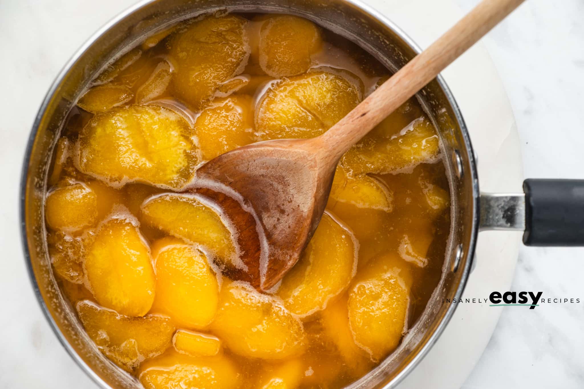 photo of ingredients to make peach simple syrup in a sauce pan with a wooden spoon mixing the ingredients