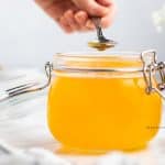 photo of peach simple syrup in a jar with a silver spoon being dipped in the syrup