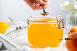 photo of peach simple syrup in a jar with a silver spoon being dipped in the syrup