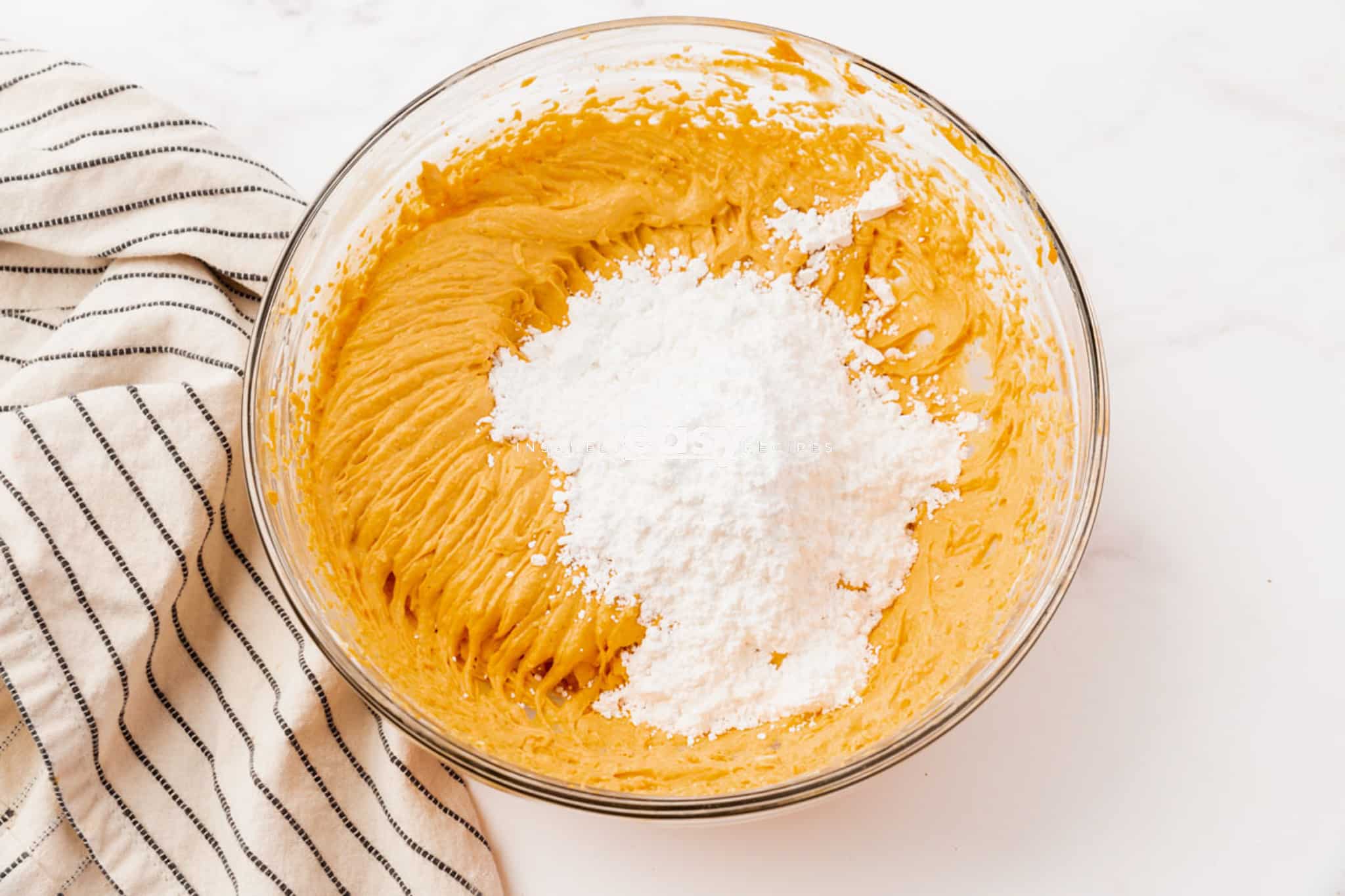 clear glass bowl with whipped orange stuff in bowl and flour on top of mixture
