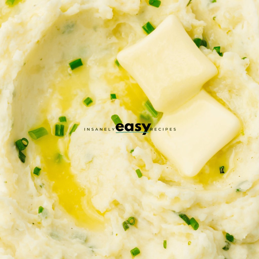 creamy ranch mashed potatoes in a white bowl. Potatoes have green seasoning on top and two butter pads