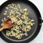 top view photo of chopped onions in a frying pan, that are golden brown, being mixed with a wooden spoon