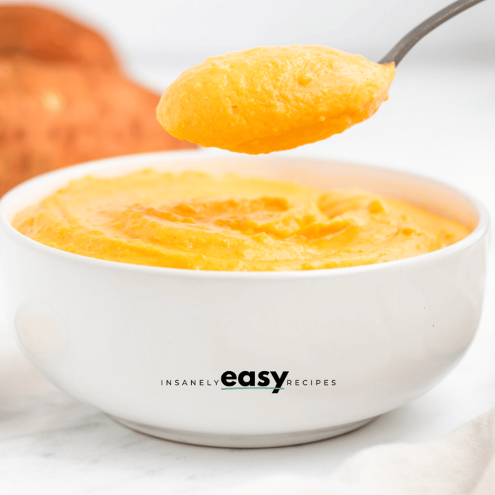 photo of sweet potato sauce in a white bowl with a spoon scooping a spoonful, with sweet potatoes in the background