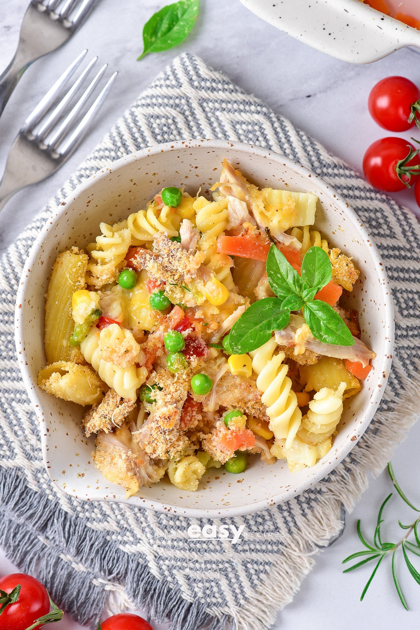 leftover turkey pasta bake in a white bowl and also in a white baking dish. You can see turkey chunks, tomatoes, basil and other veggies in the bake. Then to the back left aretwo forks and there are cherry tomatoes sprinkled around the dish.