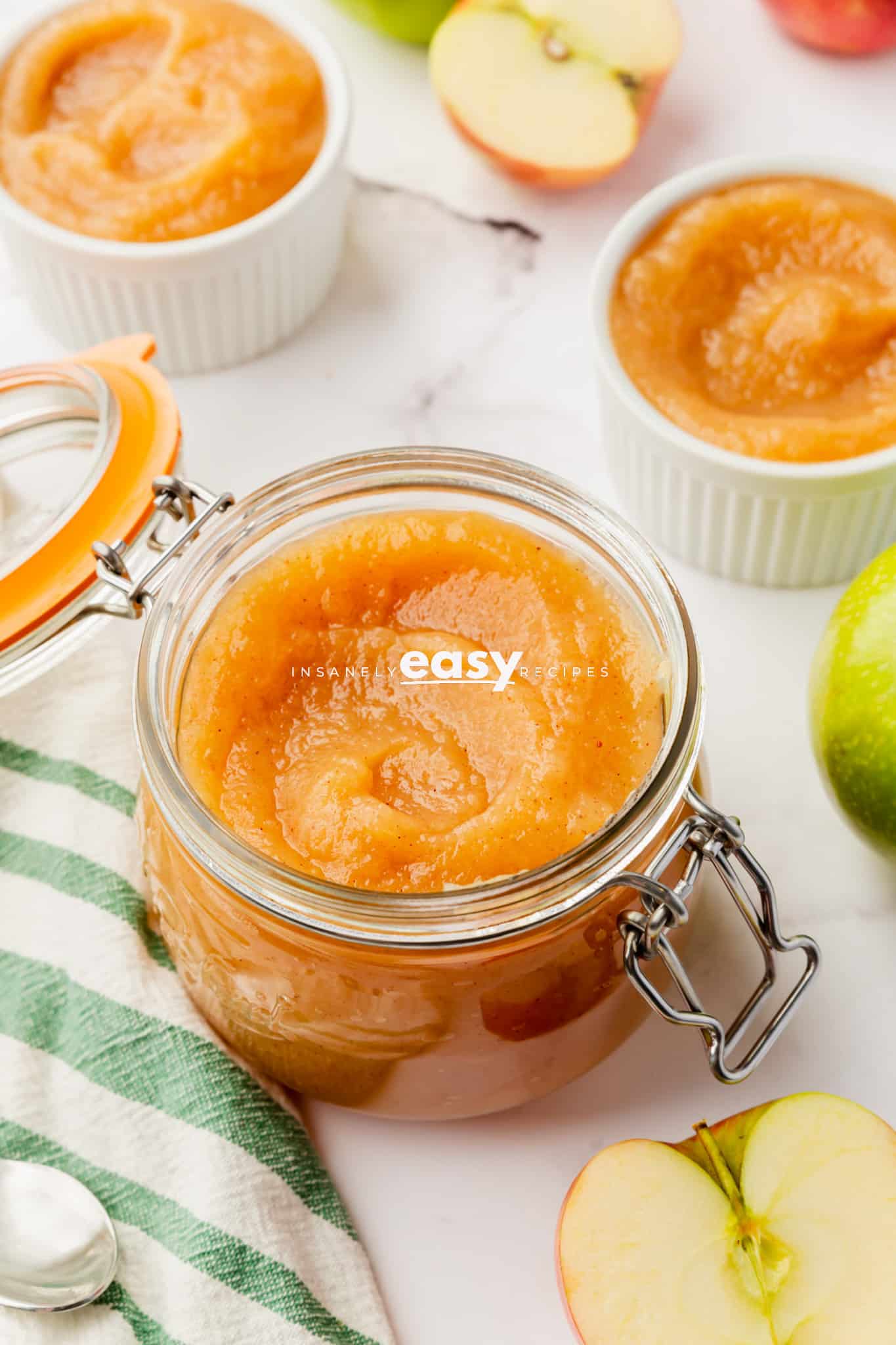 unsweetened applesauce in a clear jar with the lid open. Jar has metal latch. Bowl of applesauce to the top right.