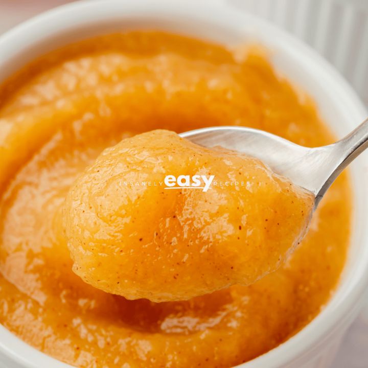cooked puree of unsweetened applesauce in a glass container, an up close shot with spoon