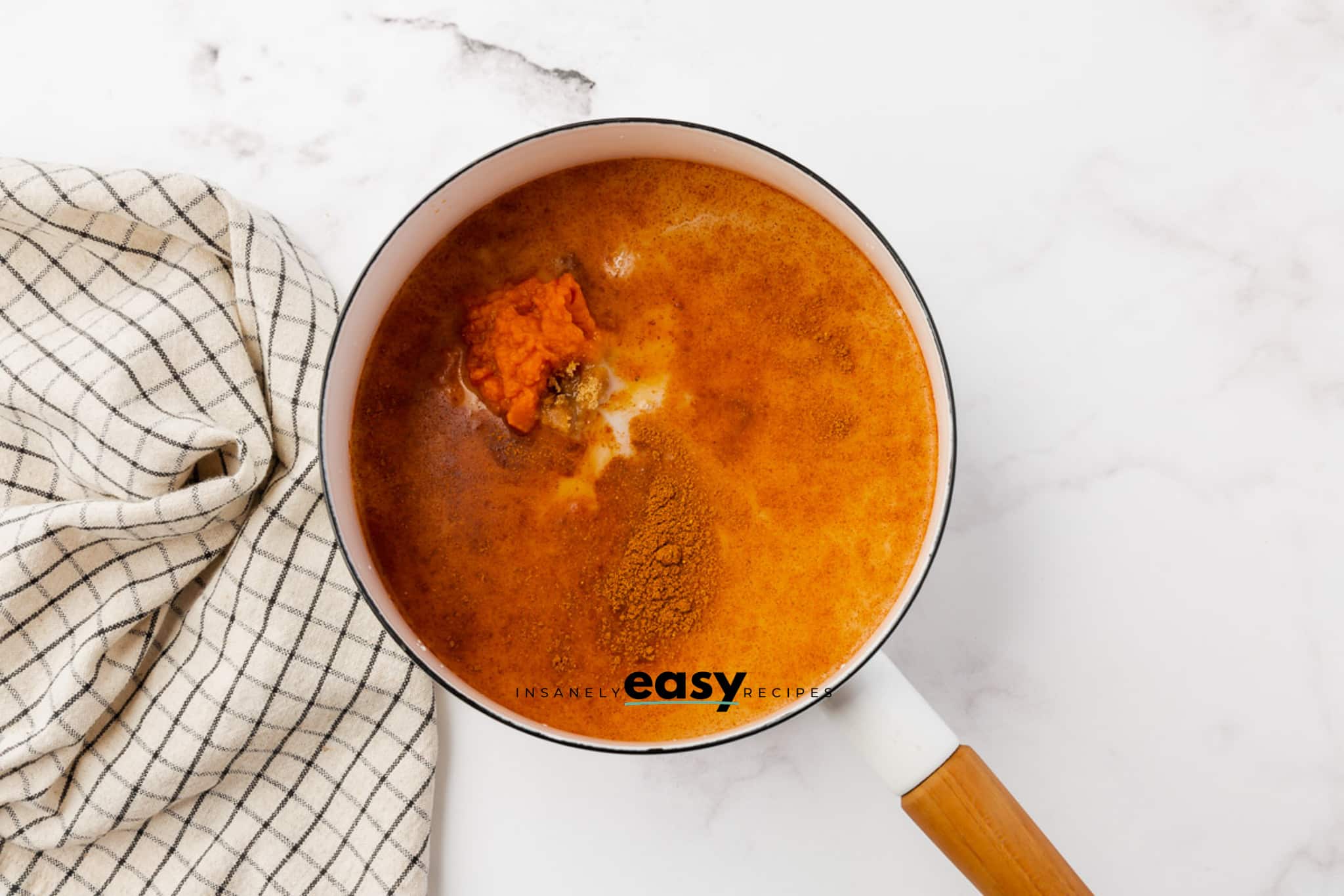 Milk, pumpkin, spices in a white enameled saucepan with wooden handle