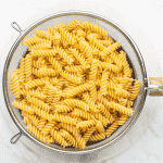a photo of fusilli pasta noodles, cooked, and in a collander over a clear glass bowl, draining