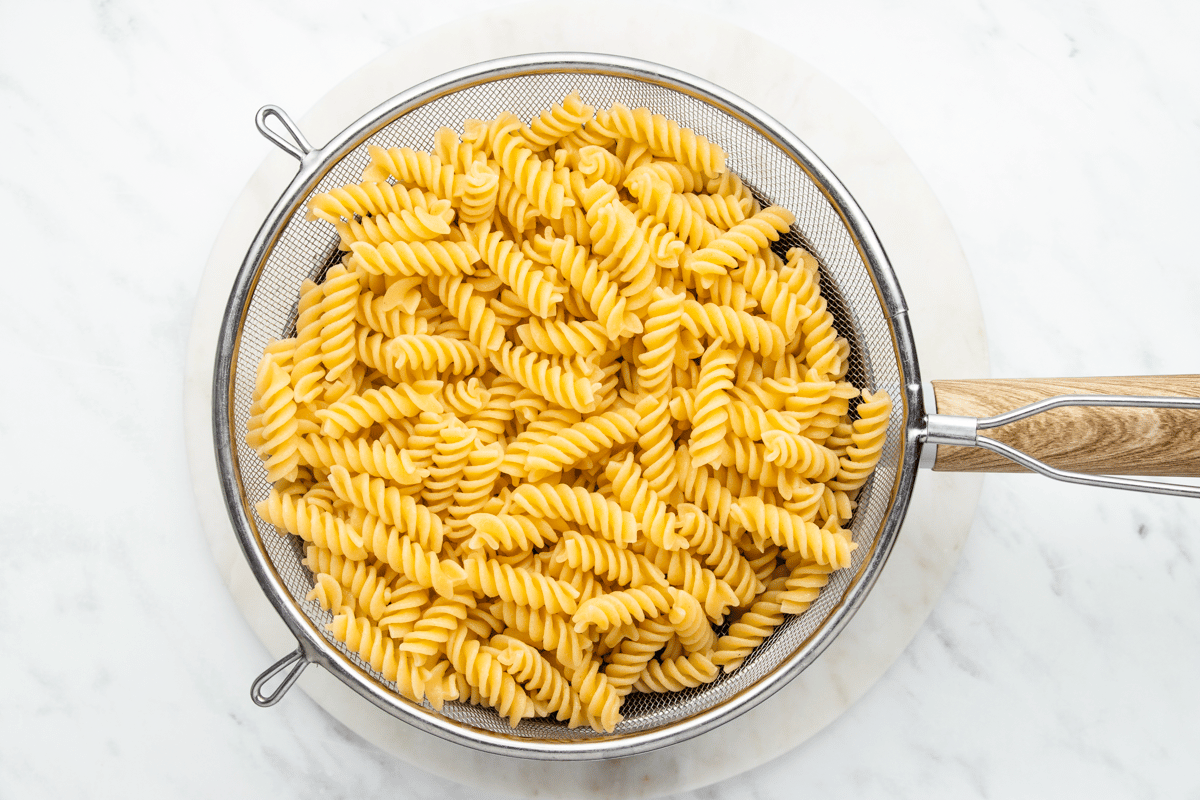 a photo of fusilli pasta noodles, cooked, and in a collander over a clear glass bowl, draining