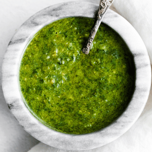 a marble bowl filled with green basil pesto. A silver spoon is in the bowl.