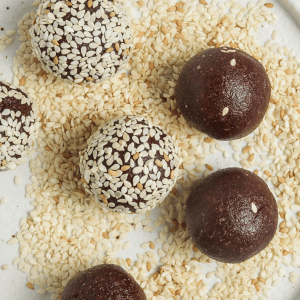 closeup photo of bliss balls, 3 coated in sesame seeds, 3uncoated, on a white plate with sesame seeds