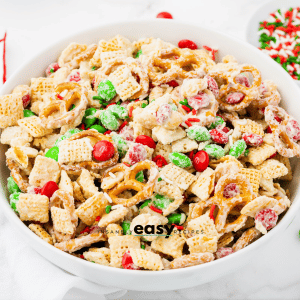 a round white bowl filled with holiday white chocolate chex mix. Sprinkles and M&ms are strewn around.