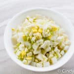 a white bowl of diced potatoes, chopped eggs, and chopped celery