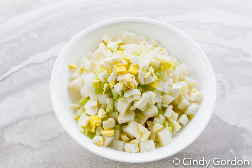 a white bowl of diced potatoes, chopped eggs, and chopped celery