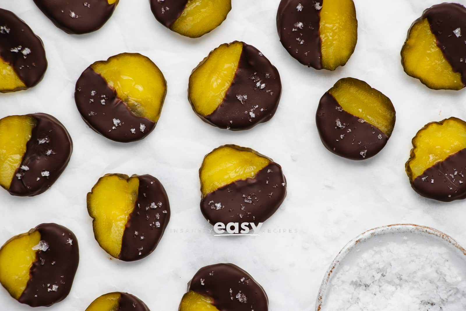 closeup photo of chocolate covered pickles with a bowl of flaky salt in the bottom right of the photo