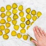 top view photo of sliced pickles on a paper towel with a hand patting them dry with a paper towel
