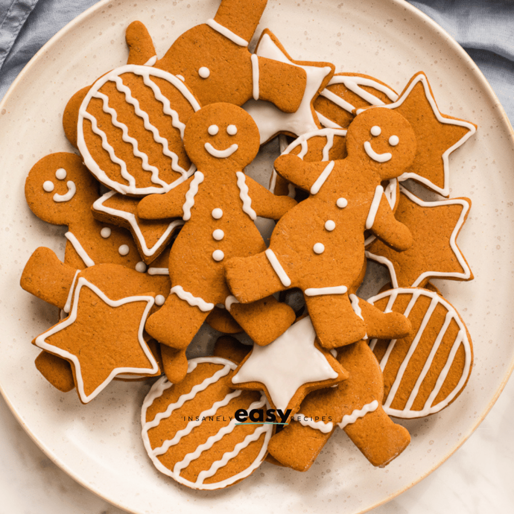 top view photo of a plate of decorated vegan gingerbread cookies in assorted holiday shapes