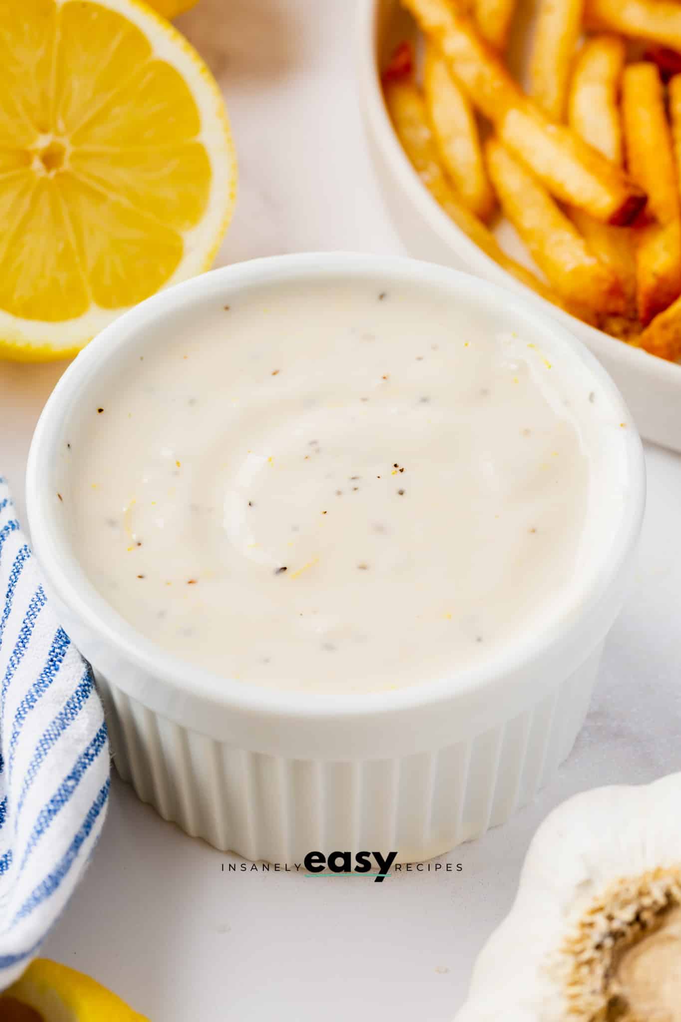 a ramekin filled with homemade lemon garlic aioli. There are french fries in the background. 