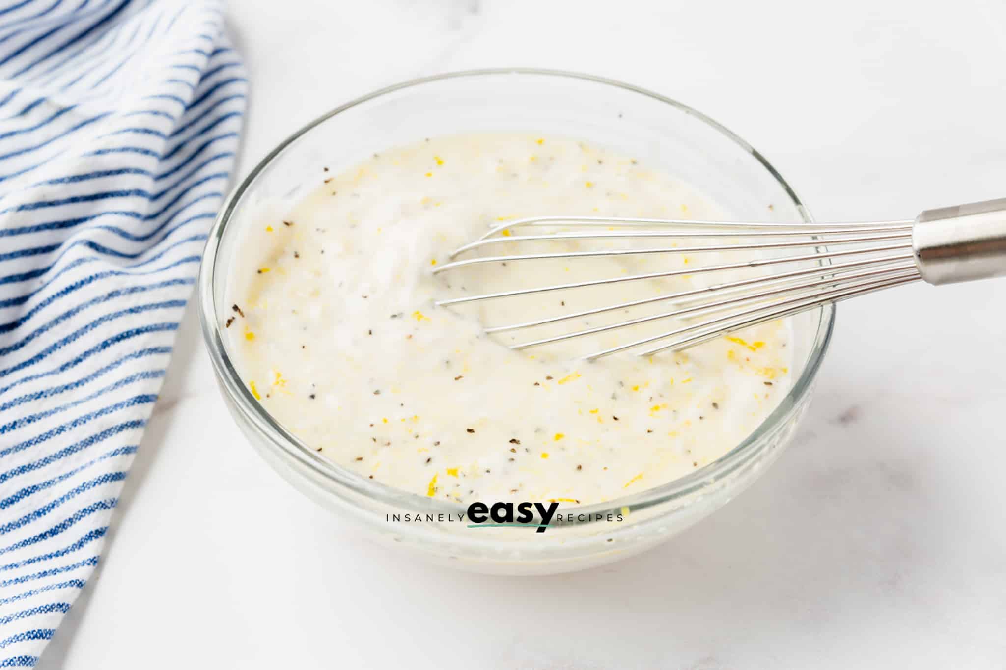 a glass bowl with lemon garlic aioli being whisked together.