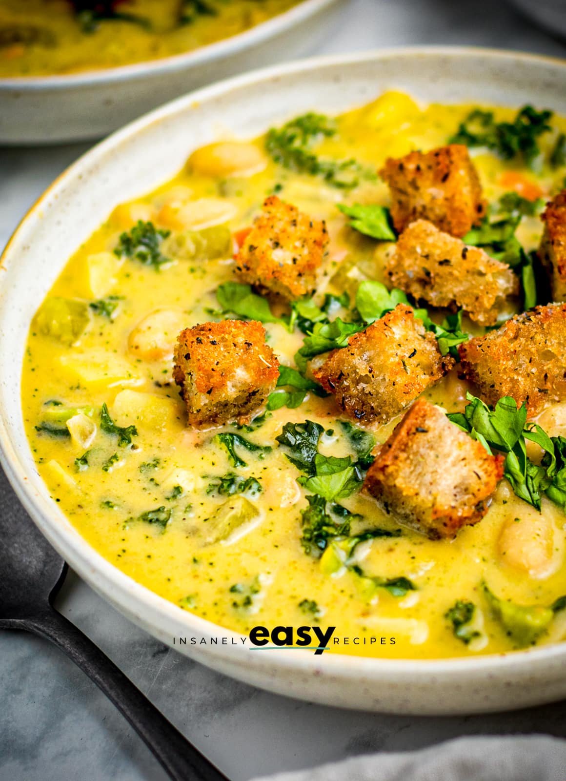 a white bowl of creamy soup topped with croutons and fresh herbs. The shot shows only the left 3/4 of the bowl. 