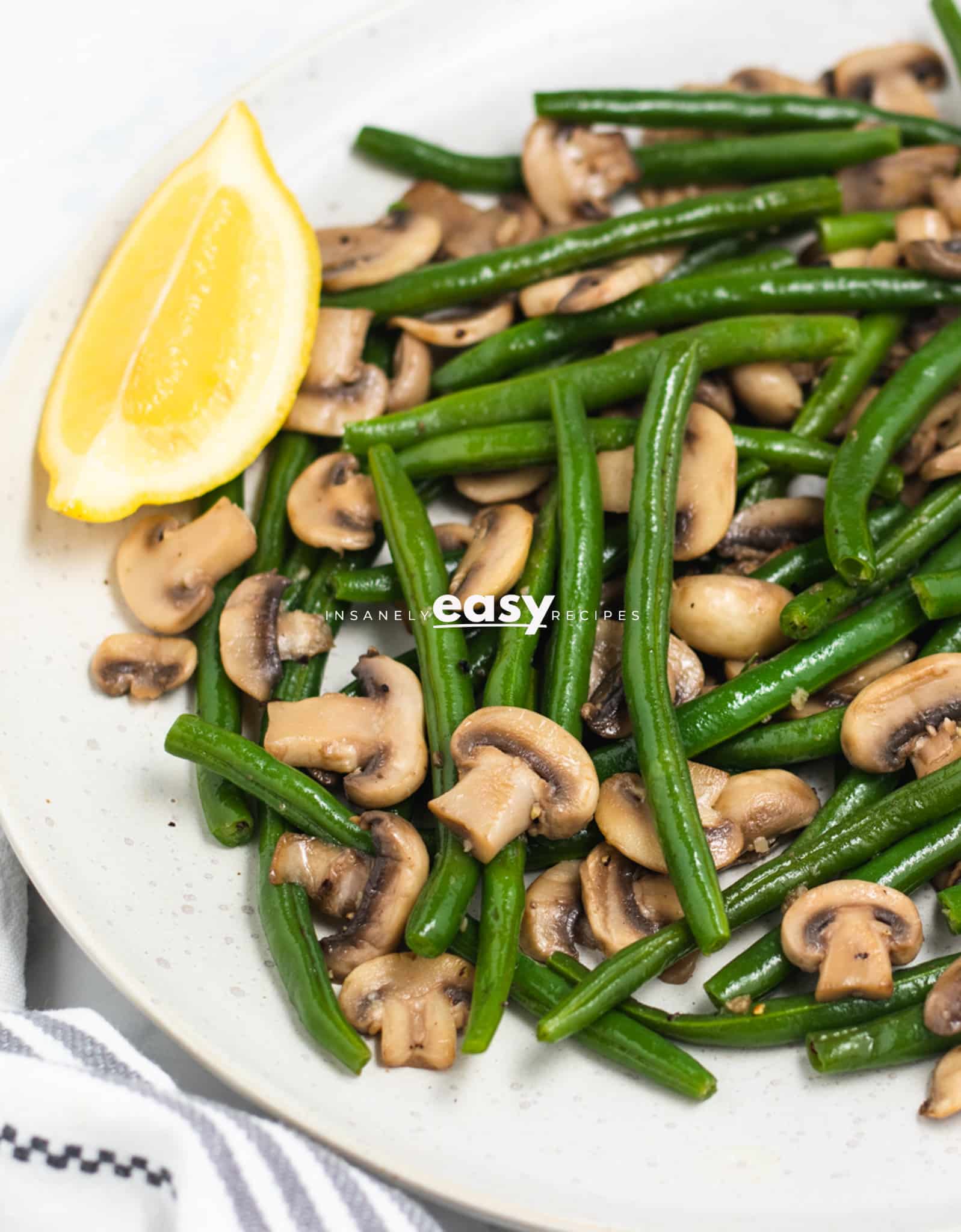 a round white plate filled with green beans and mushrooms. Three lemon wedges are around the edge of the plate.