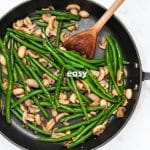 green beans and mushrooms sauteed in a frying pan with a wooden spoon.