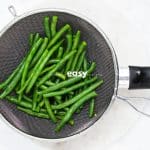 blanched green beans in a mesh strainer, viewed from above.